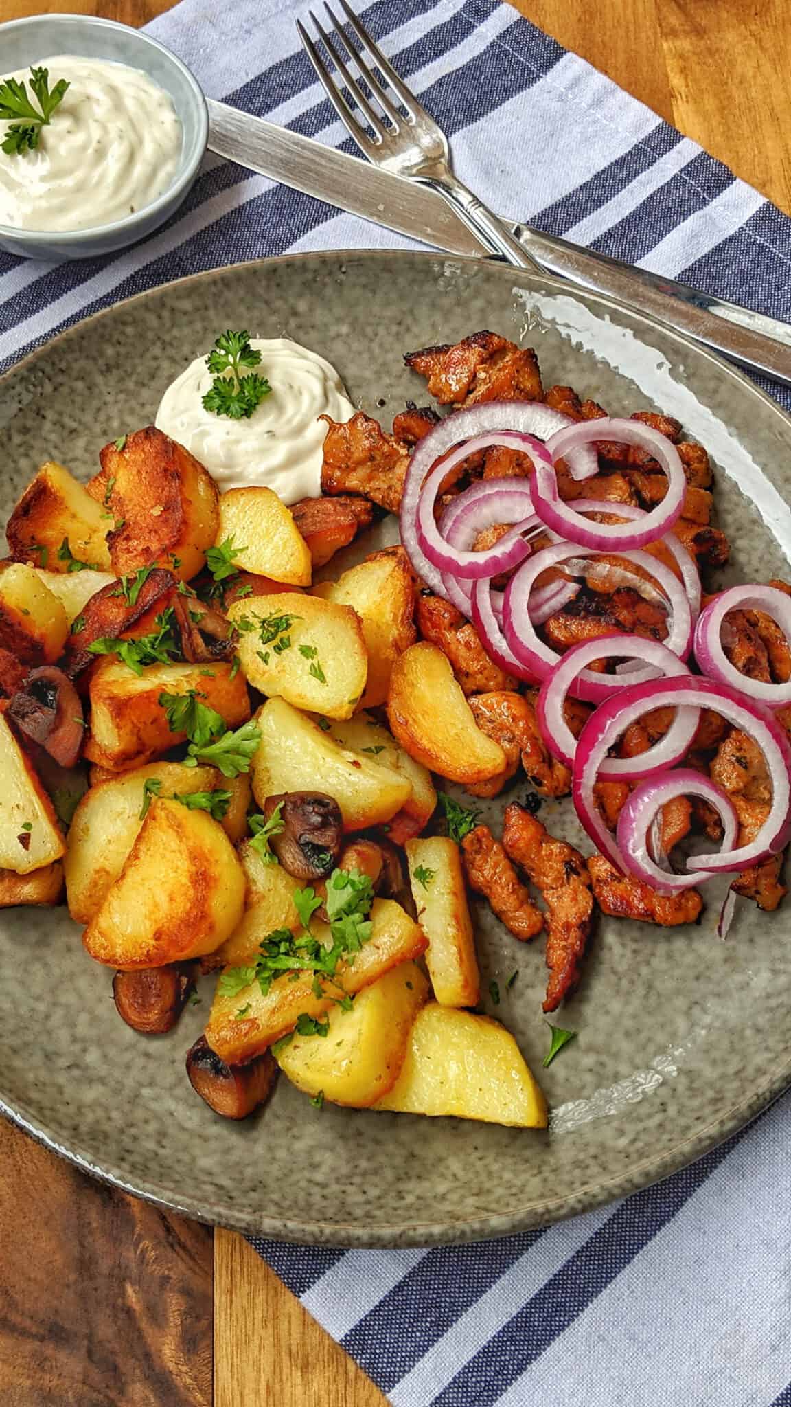 Ein dunkler Teller mit Bratkartoffeln und Gyros.