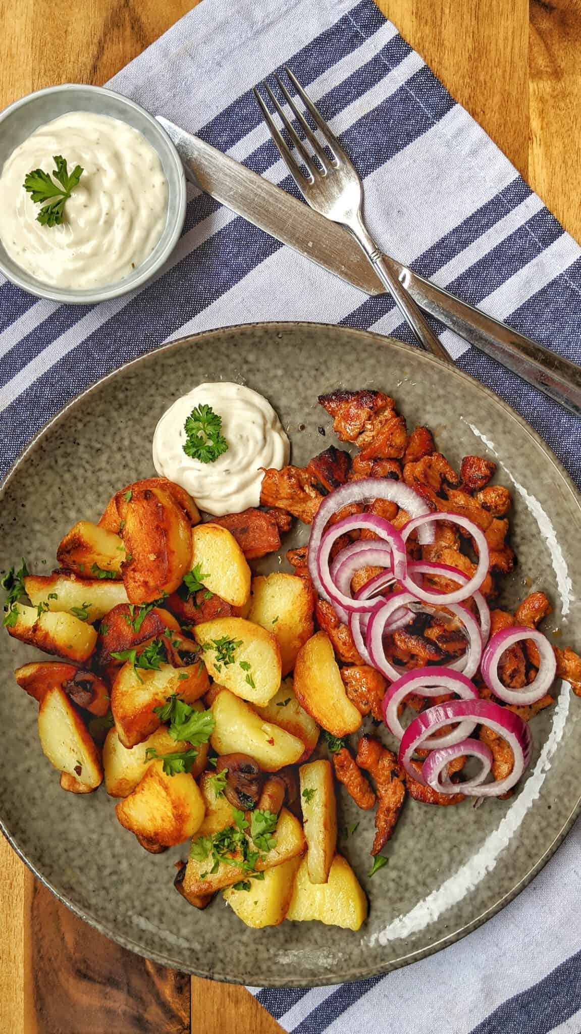 Ein dunkler Teller mit Bratkartoffeln und Gyros.