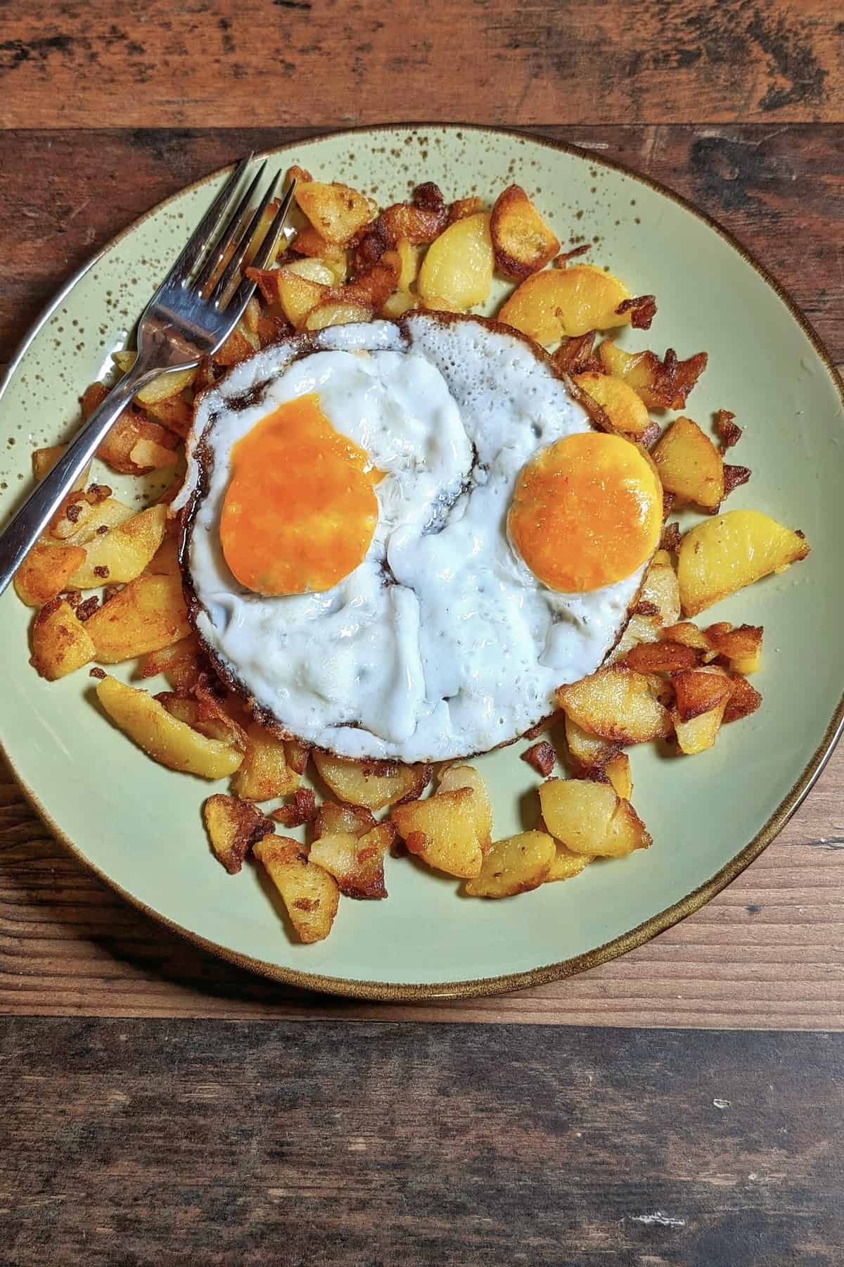 Ein Teller mit Bratkartoffeln und zwei Spiegeleiern.