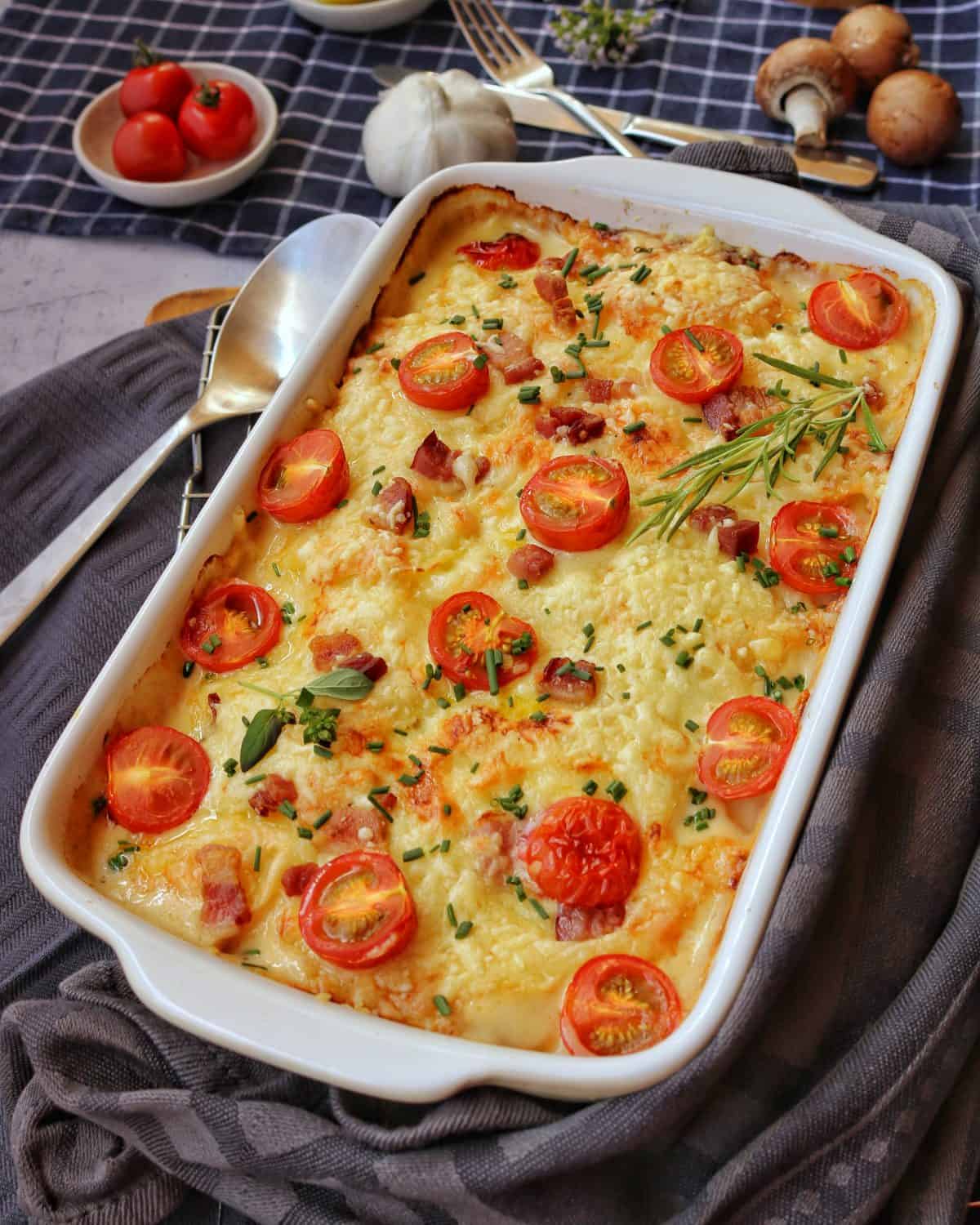 Eine weisse Auflaufform mit Kartoffel-Kohlrabi-Gratin mit Tomaten.