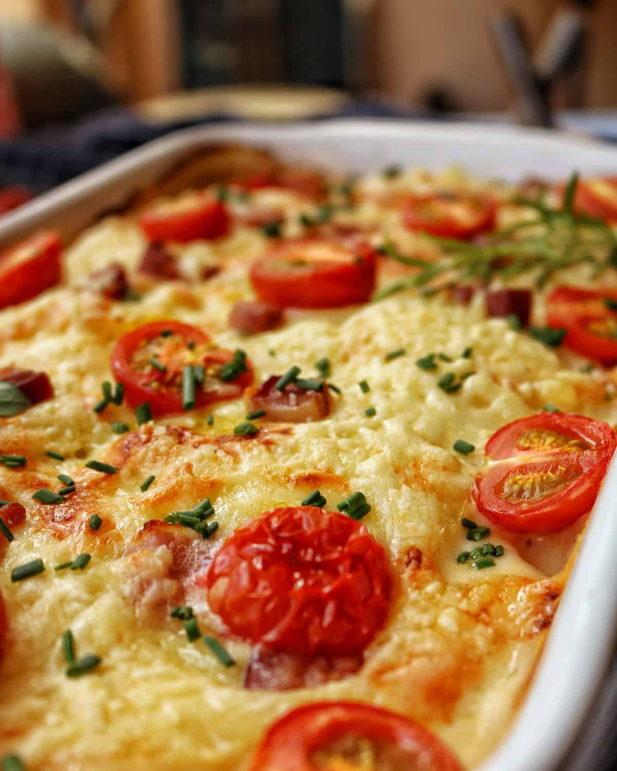 Eine Nahaufnahme einer weissen Auflaufform mit Kartoffel-Kohlrabi-Gratin mit Tomaten.