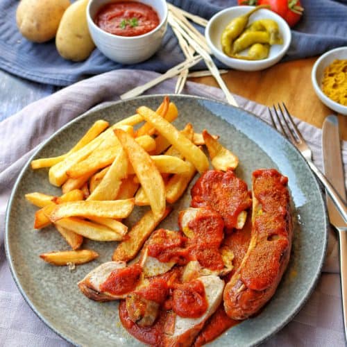 Ein Teller mit Currywurst und Pommes. Darüber Deko.