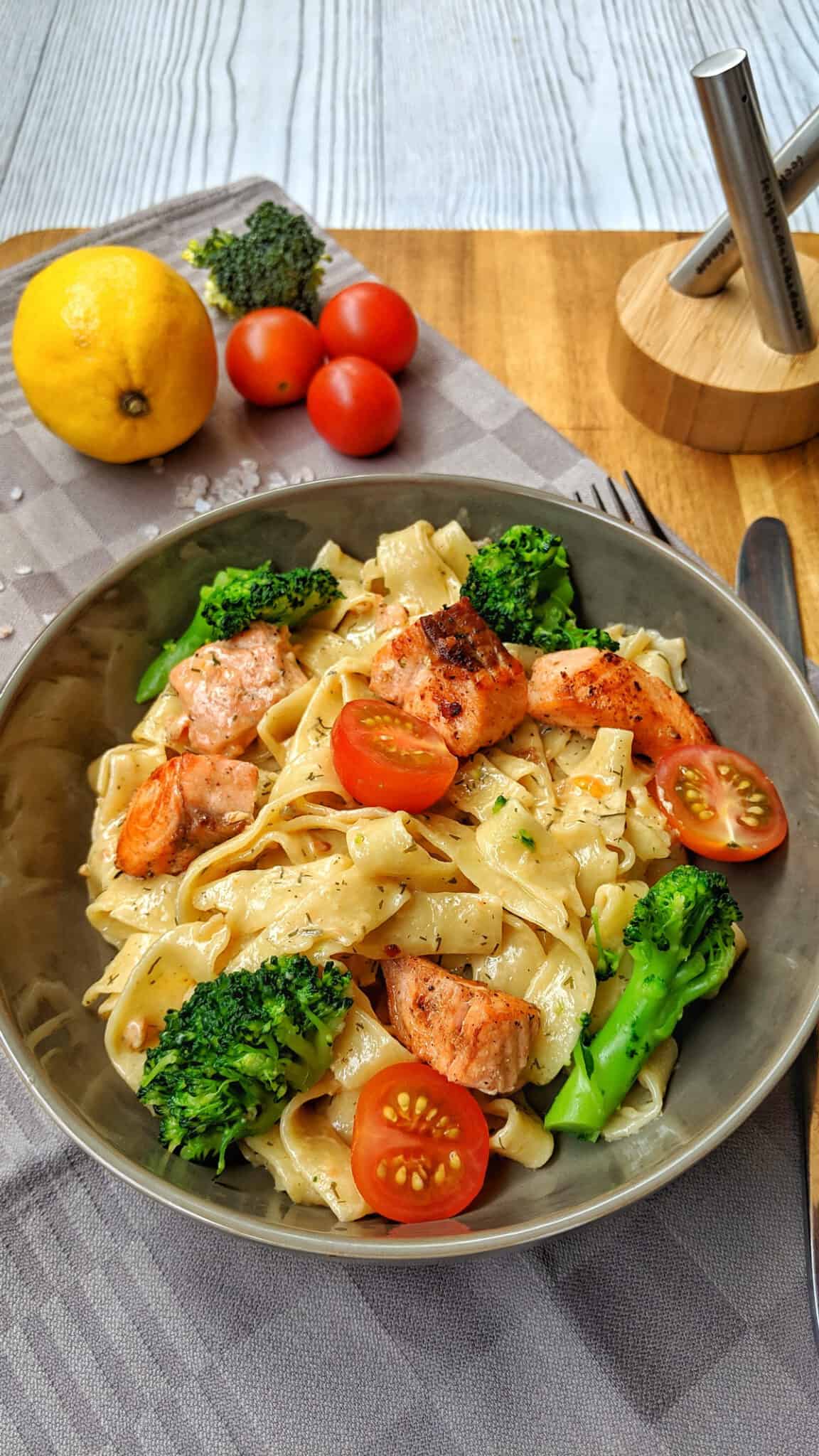 Ein Teller mit Nudeln und Lachs in Sahnesoße mit Brokkoli und Tomaten.