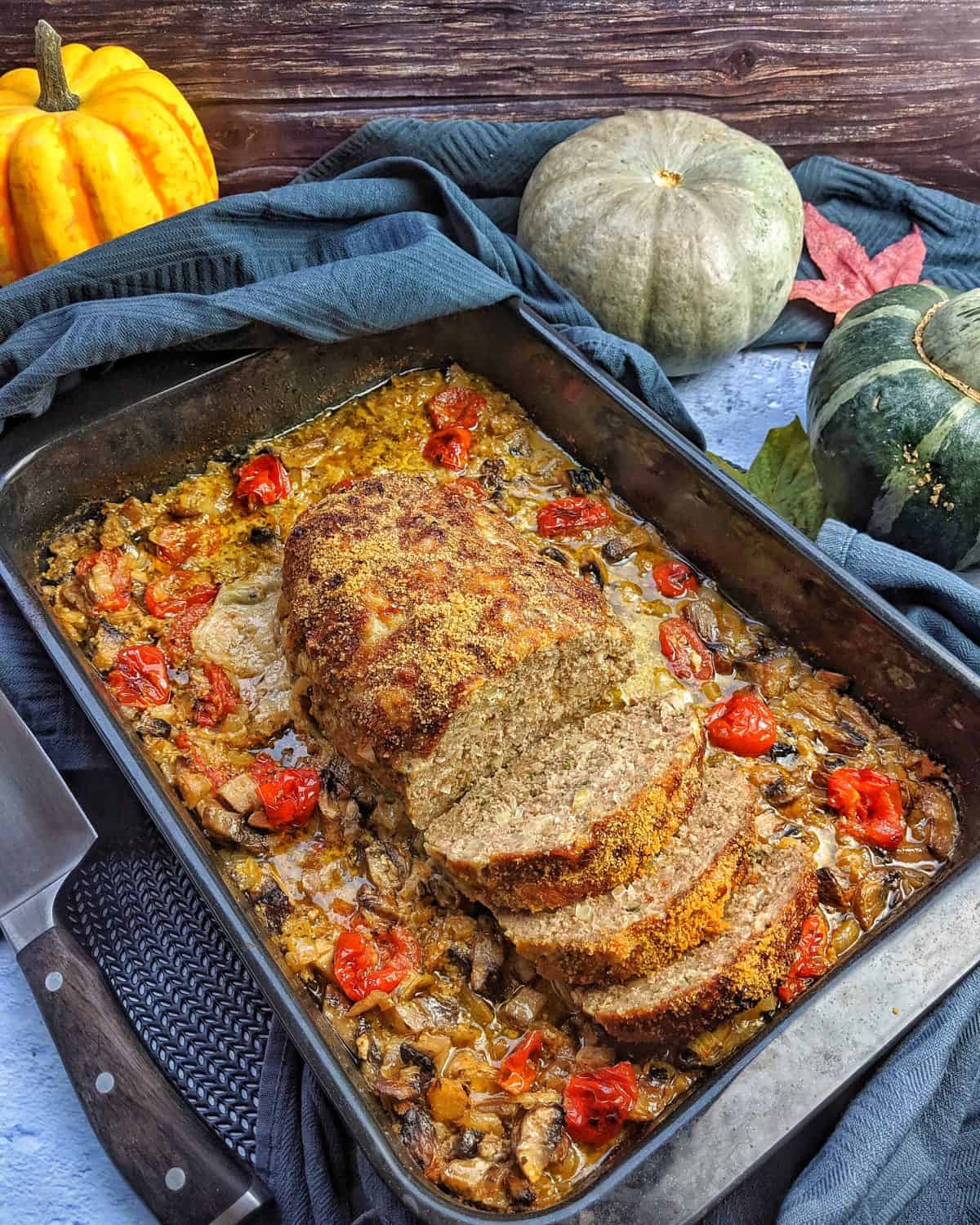 Hackbraten aufgeschnitten in einer Auflaufform mit Tomaten und Pilzen.