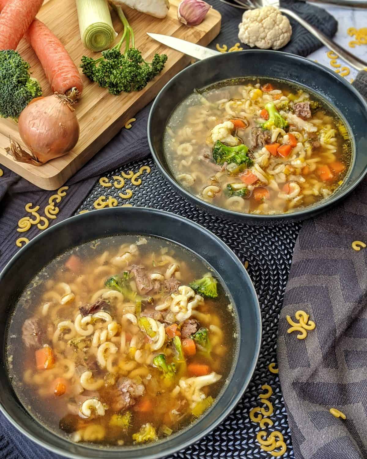 Zwei dunkle tiefer Teller mit Nudelsuppe mit Rindfleisch. Im Hintergrund Deko.