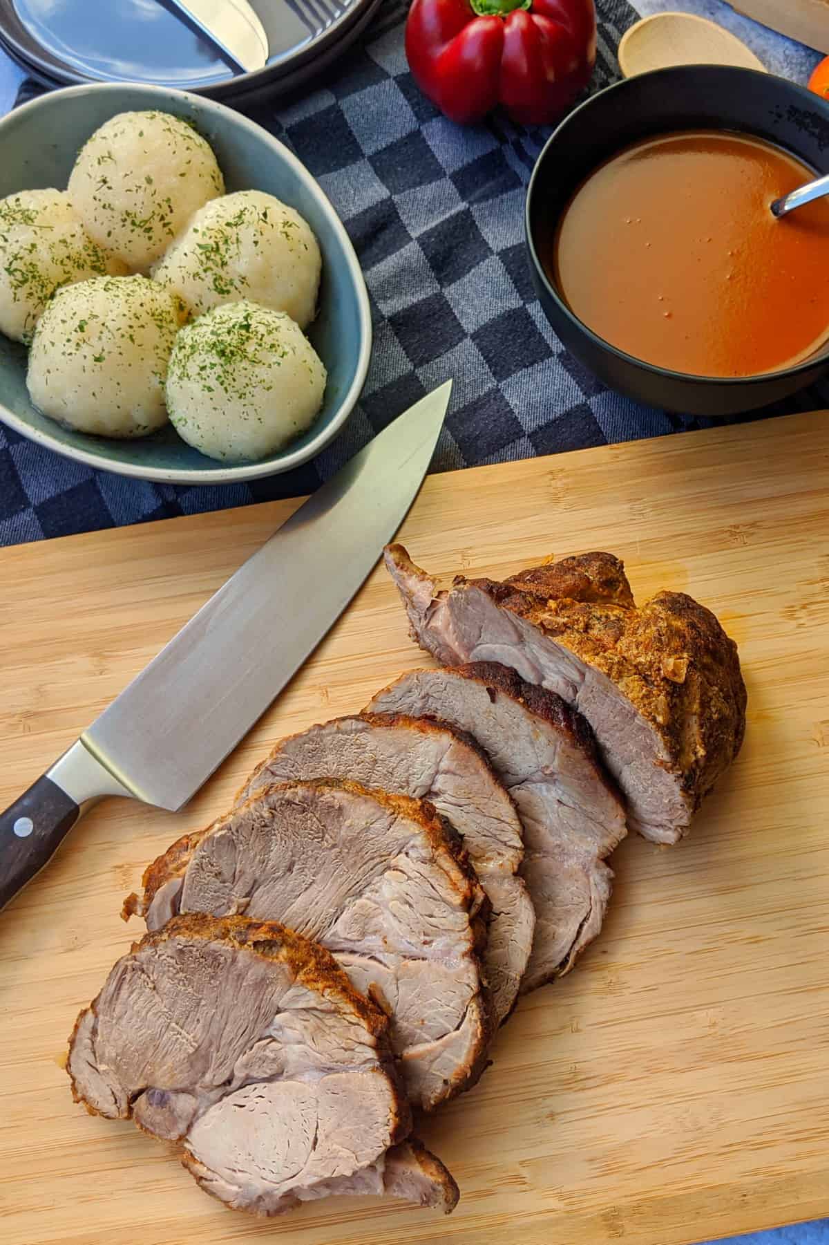 Ein angeschnittener Schweinebraten auf einem Holzbrett. Im Hintergrund Klöße und Bratensoße.