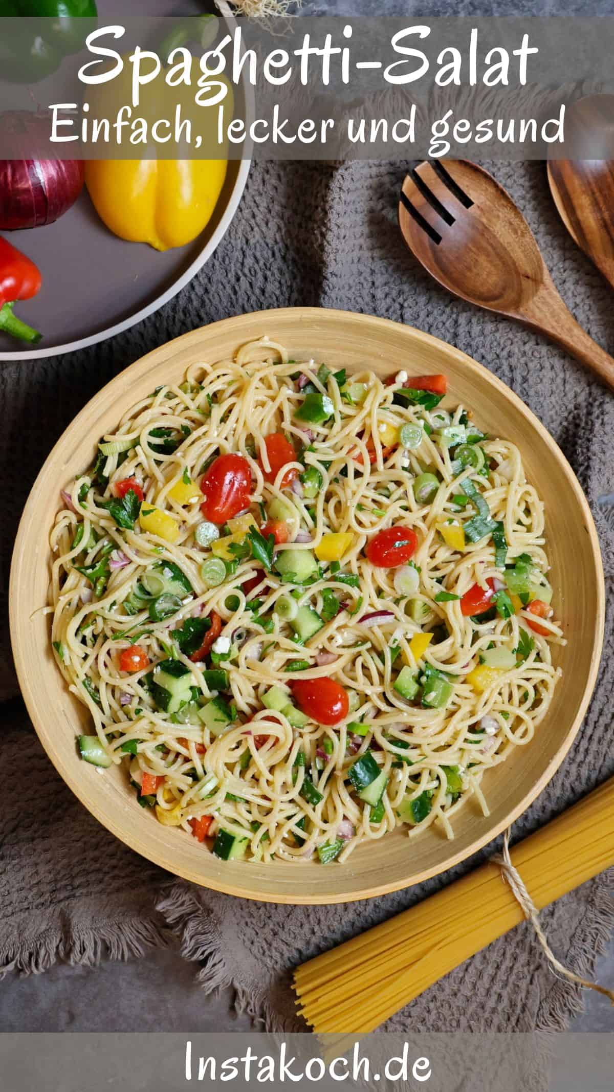 Eine Schüssel mit Spaghetti-Salat. Darüber ein Teller mit Gemüse und ein Salatbesteck.
