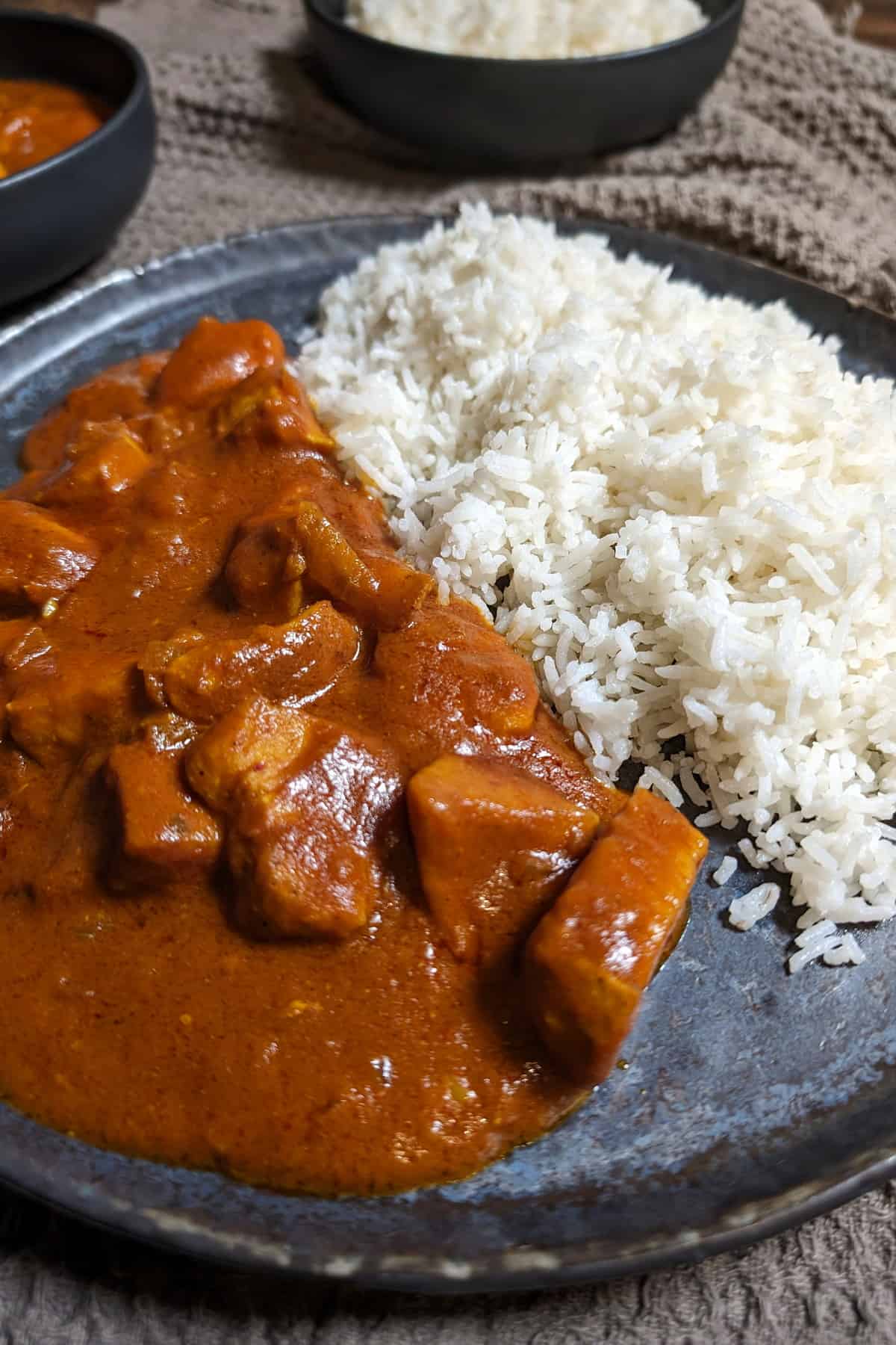 Eine Nahaufnahme von einem Teller mit Hähnchen-Curry und Reis. Darüber eine Schale mit Hähnchen-Curry und eine Schale mit Reis.