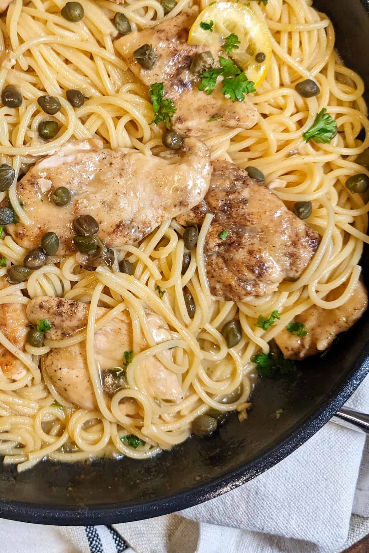 Eine Nahaufnahme einer Pfanne mit Chicken Piccata mit Spaghetti.