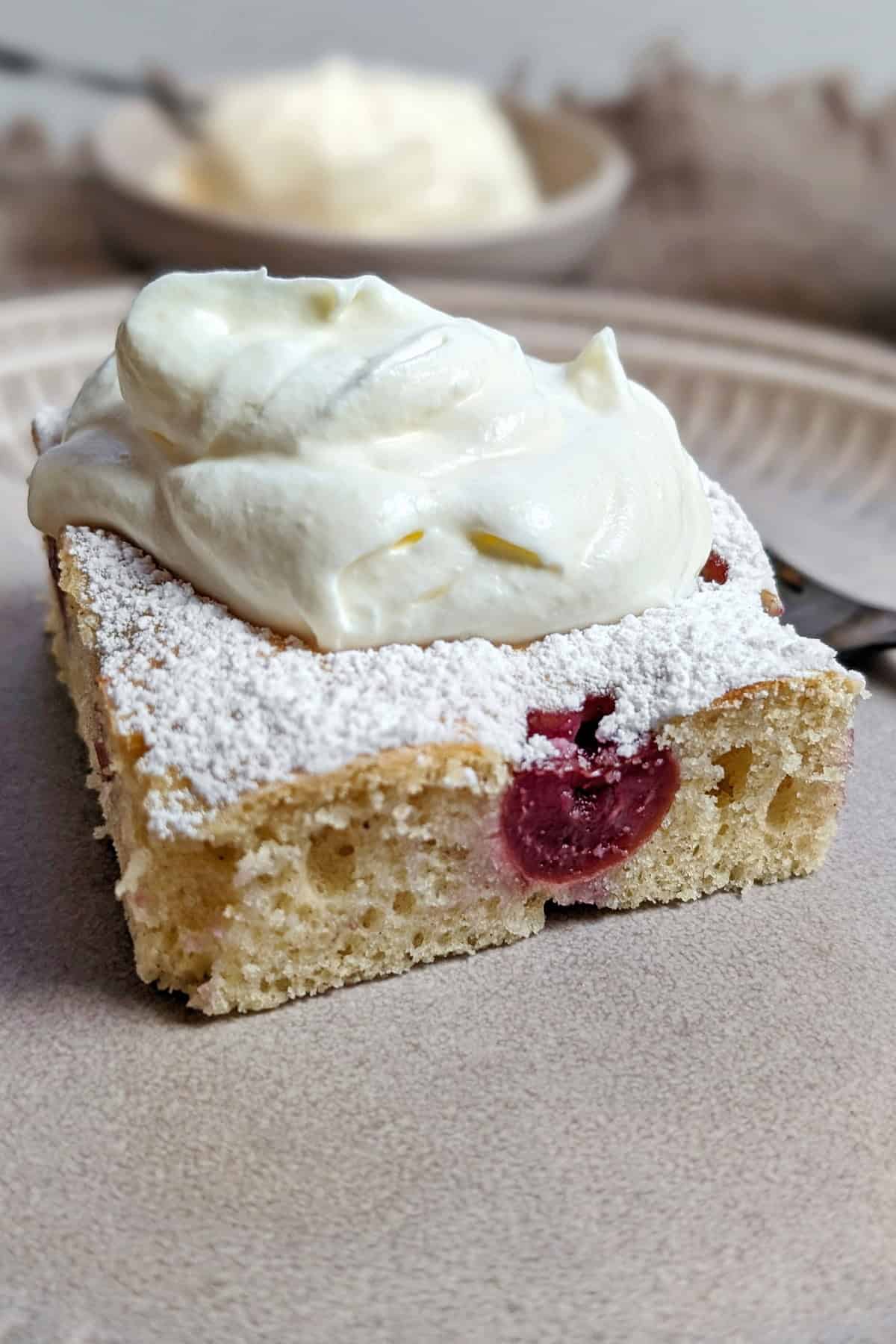 Ein Stück Blitzkuchen mit Sauerkirschen mit Schlagsahne auf einem Teller.