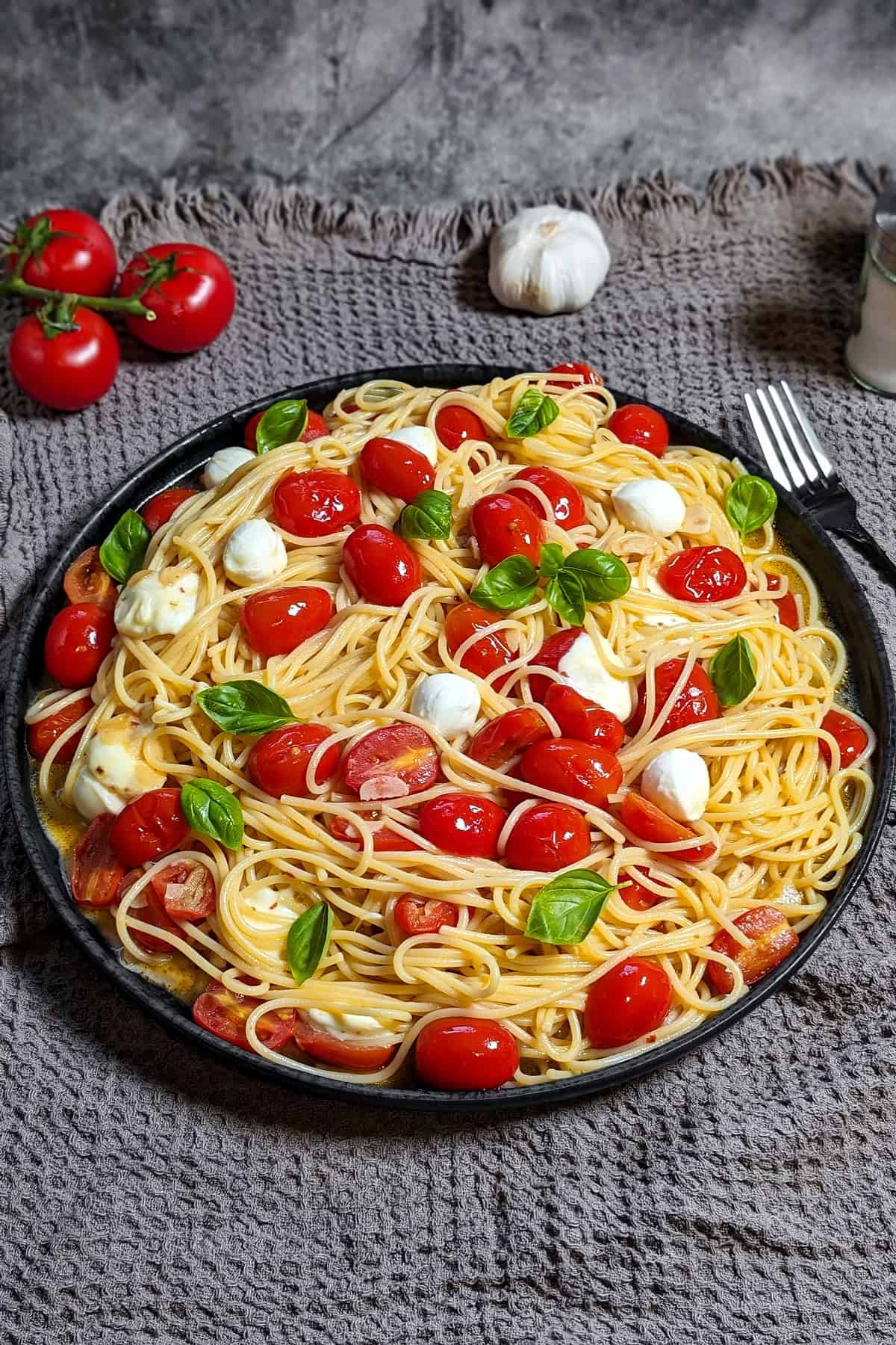 Eine dunkle runde Servierplatte mit Caprese Pasta.