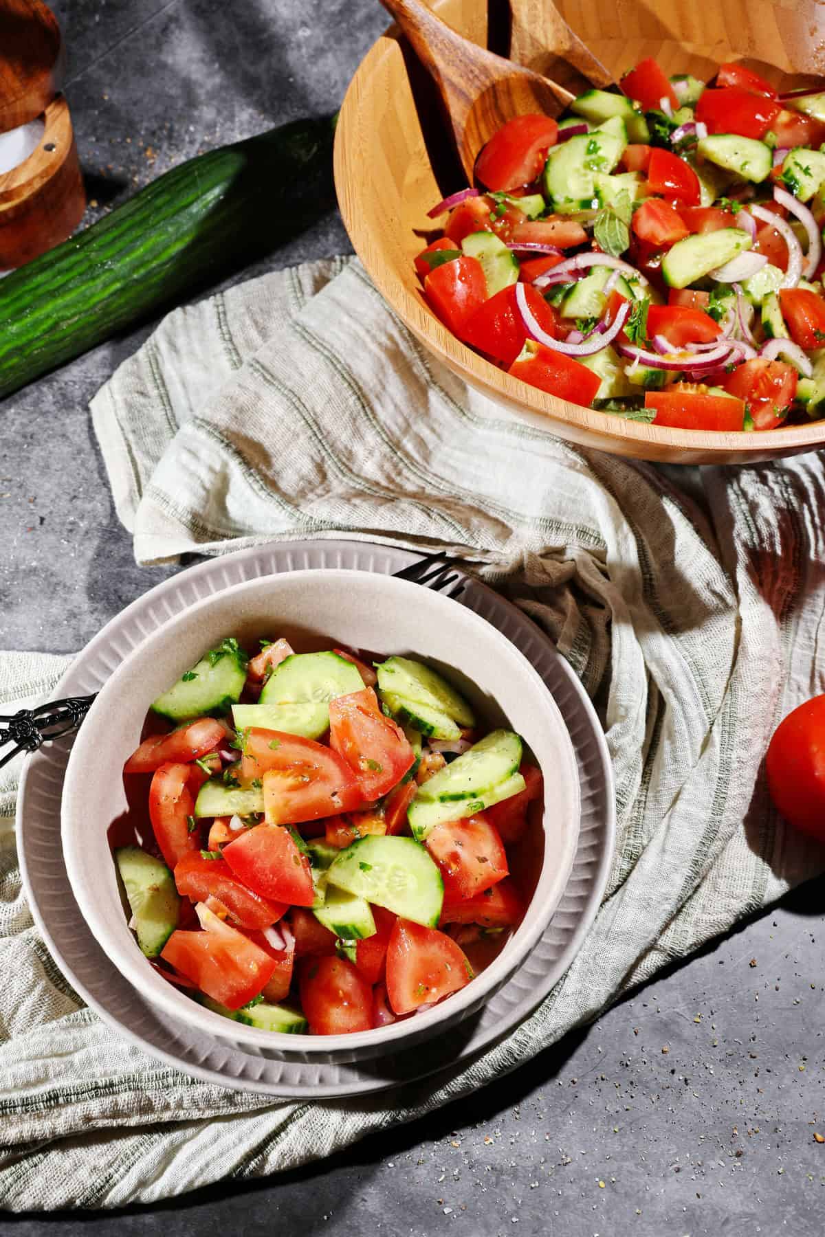 Ein Schälchen mit Tomaten-Gurke Salat. Darüber eine Salatschüssel mit dem übrigen Salat.