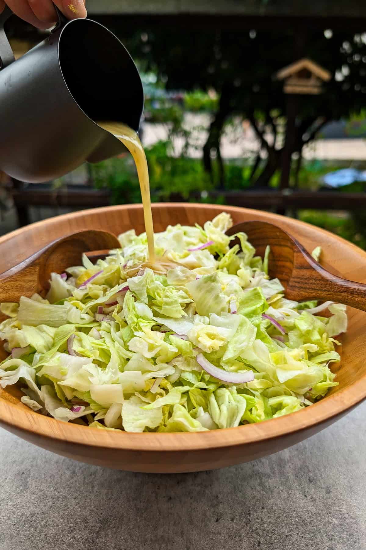 Eine Salatschüssel mit grünem Salat mit Honig-Senf Dressing in die Dressing gegossen wird.