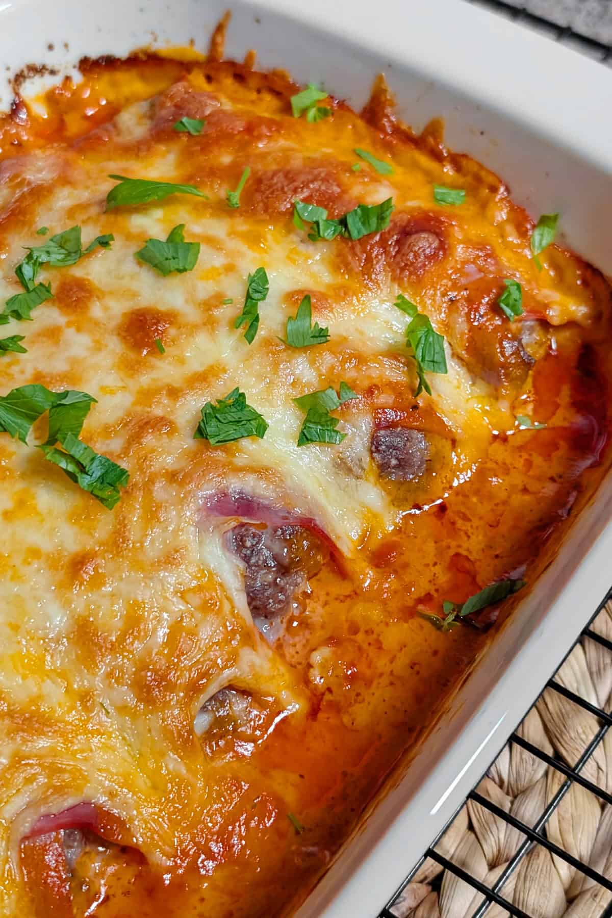 Eine Nahaufnahme einer weißen Auflaufform mit Käse überbackenen Schinken-Hack-Röllchen in Tomatensoße.