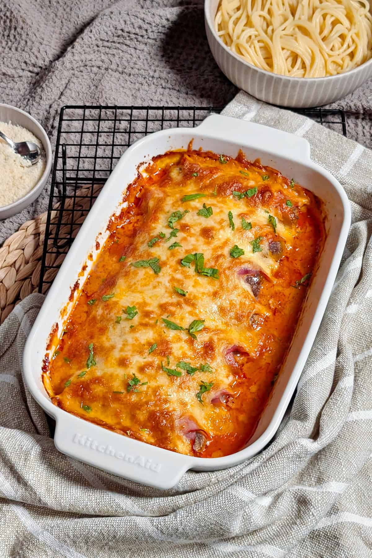 Eine weiße Auflaufform mit Käse überbackenen Schinken-Hack-Röllchen in Tomatensoße.