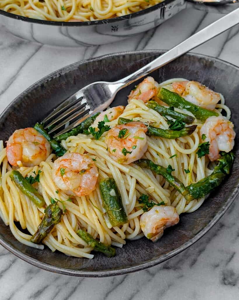 Ein ovalförmiger Teller mit Spaghetti mit Garnelen und grünem Spargel.