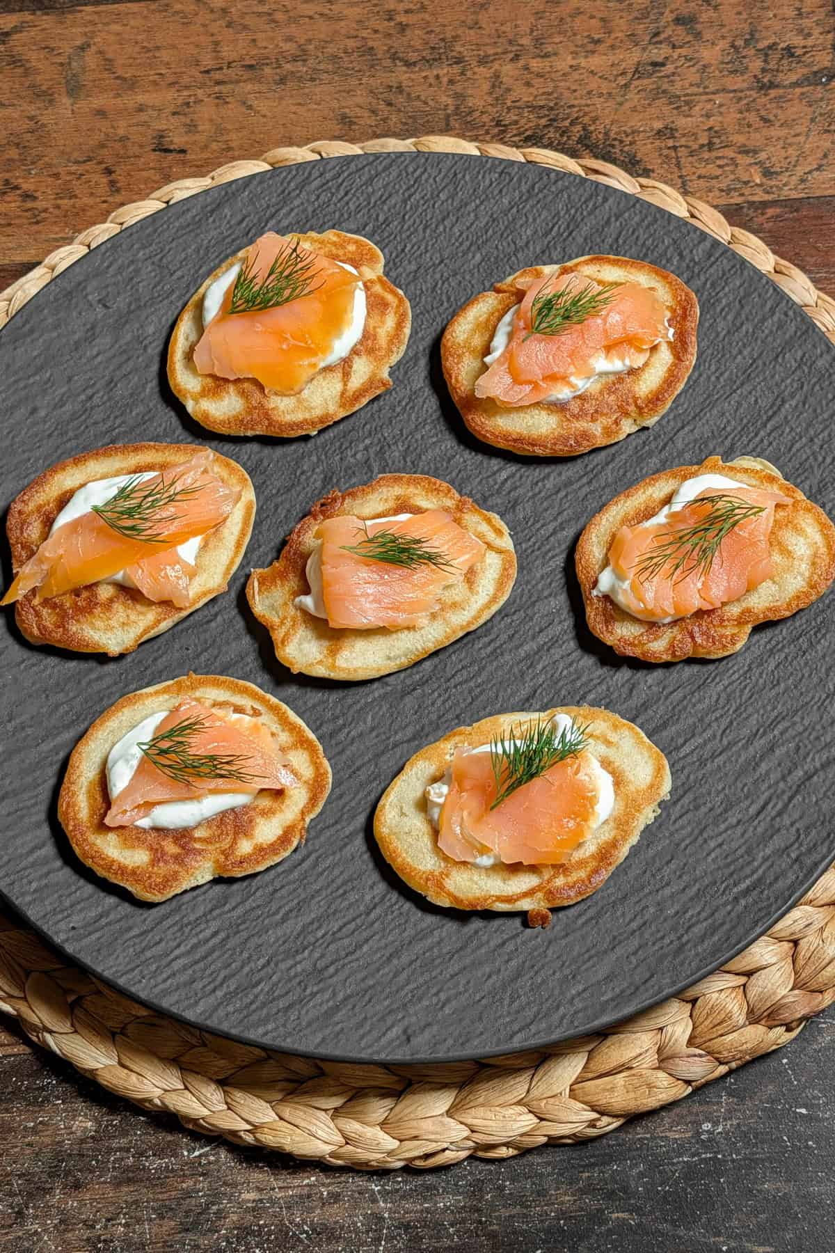 Eine Servierplatte mit Blinis mit saurer Sahne, Lachs und Dill.